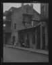 Arnold Genthe / View from across street of a man and child sitting on steps and a woman walking down sidewalk in the French Quarter, New Orleans / between 1920 and 1926