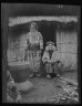 Arnold Genthe / Ainu man and seated woman at the entrance of a hut / 1908