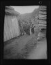 Arnold Genthe / Group of Ainu children standing in a passageway between huts / 1908