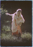 Arnold Genthe / Woman wearing a costume, including a frilled cap, holding a fan and taking a bow, outdoors / between 1906 and 1942
